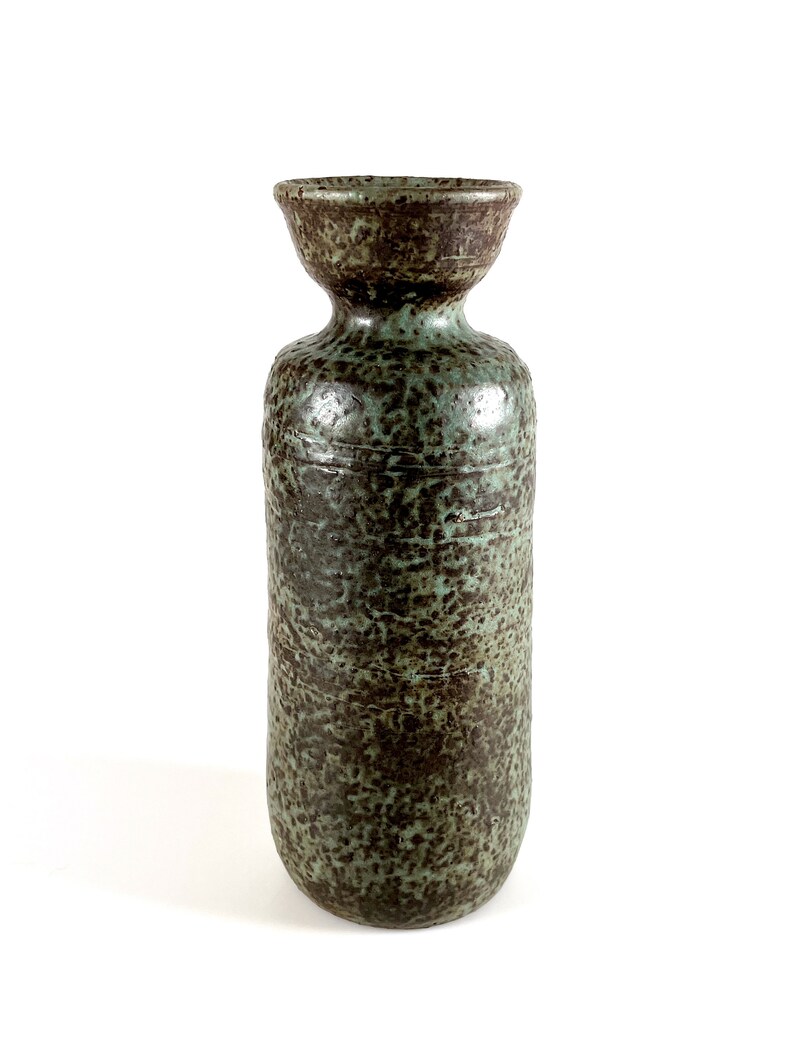K&ouml;nnte beinhalten: Eine hohe, zylindrische Keramikvase mit einem gesprenkelten gr&uuml;n-braunen &Uuml;berzug. Die Vase hat eine leicht ausgestellte &Ouml;ffnung oben.