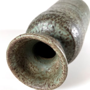 K&ouml;nnte beinhalten: Eine gr&uuml;ne und braune Keramikvase mit einem breiten, ausgestellten Boden und einem schmalen Hals. Die Vase hat eine gesprenkelte Glasur.