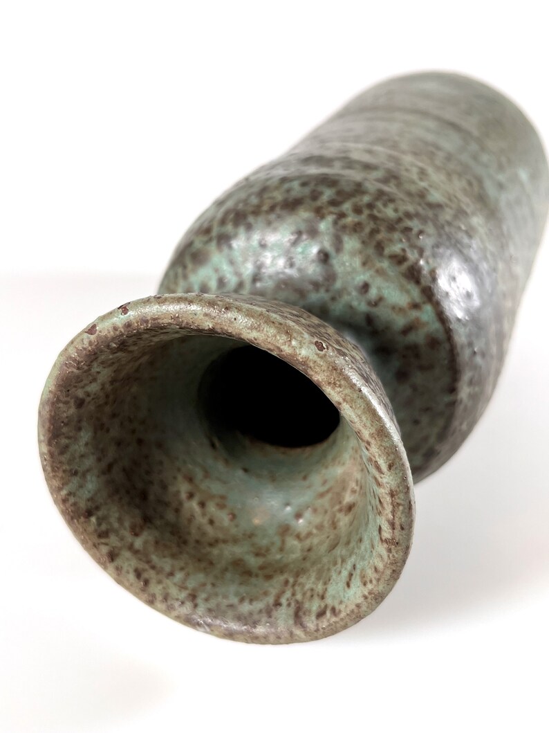 K&ouml;nnte beinhalten: Eine gr&uuml;ne und braune Keramikvase mit einem breiten, ausgestellten Boden und einem schmalen Hals. Die Vase hat eine gesprenkelte Glasur.