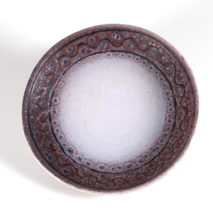 May include: A white ceramic bowl with a brown and purple rim. The rim has a decorative pattern of circles and swirls.