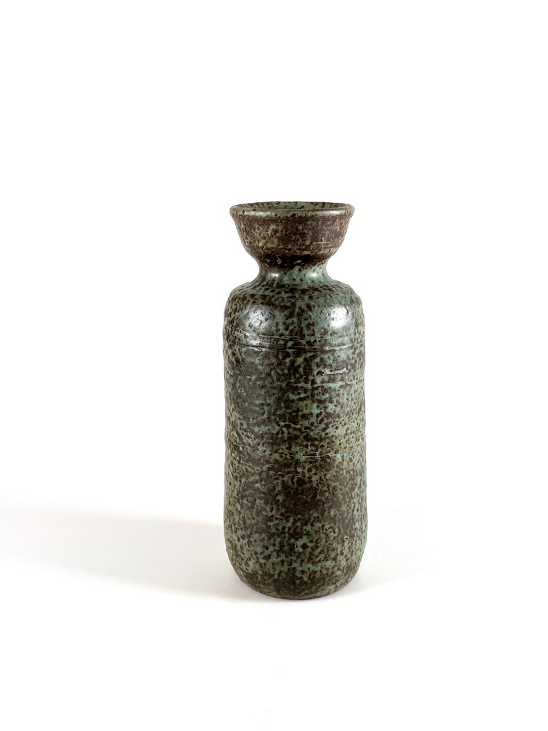 K&ouml;nnte beinhalten: Eine hohe, gr&uuml;ne Keramikvase mit einer gesprenkelten braunen Glasur. Die Vase hat einen breiten, abgerundeten Boden und einen schmalen Hals.