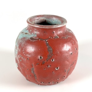 May include: A small, round, red ceramic vase with a textured surface and a light blue glaze. The vase has a wide opening and is ideal for displaying small flowers or plants.