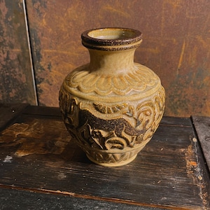 Peut inclure: Un petit vase en céramique avec un glaçage brun et beige. Le vase a un corps rond et un col étroit. Il est décoré d'un motif en relief de fleurs et de feuilles stylisées.