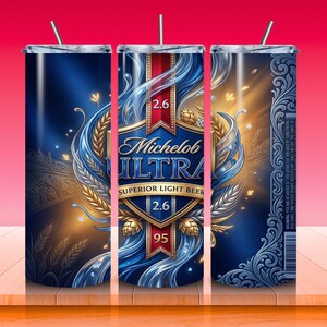 May include: A stainless steel tumbler featuring a blue and gold design with the words "Michelob Ultra Superior Light Beer". The design includes wheat, water, and the numbers "2.6" and "95". The tumbler has a silver straw.