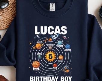 Puede incluir: Una sudadera azul marino de manga larga con un gráfico del sistema solar y el número 5 en el centro. El texto dice LUCAS BIRTHDAY BOY, e incluye etiquetas para Mercurio, Venus, Tierra, Marte, Júpiter, Saturno, Urano y Neptuno.