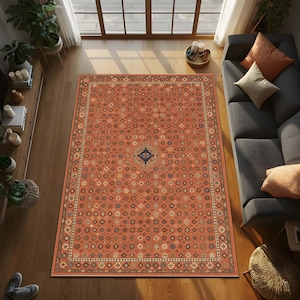 May include: An overhead shot of a rectangular, patterned rug in a living room setting. The rug is predominantly orange with a detailed geometric design, bordered by a cream and brown pattern. The room includes a gray sofa, wooden floors, and natural light.