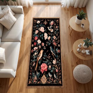May include: A rectangular black rug with a floral and bird design. The rug features pink and white flowers, green leaves, and birds in various colors. The border is a dark gold color.