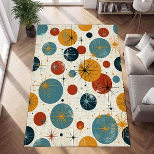 May include: A rectangular area rug with a mid-century modern design. The rug features a cream-colored background with a pattern of colorful circles and starbursts in shades of orange, blue, and black. The rug is placed on a hardwood floor.