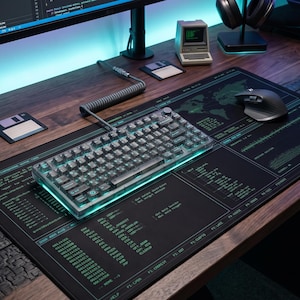 May include: A black desk mat featuring a green digital world map and technical code patterns, topped with a transparent mechanical keyboard with a coiled cable, a dark grey wireless mouse, two floppy disks, and a miniature computer model.