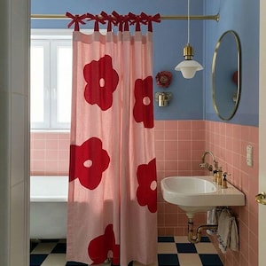 Puede incluir: Una cortina de ducha de color rosa claro con grandes motivos florales rojos y lazos de tela roja que cuelgan de una barra de latón. La cortina está situada en un baño con paredes de azulejos azules y rosas y un suelo de cuadros azules y blancos.