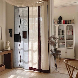 Puede incluir: Una habitación con una paleta de colores neutros, con una ventana cubierta por una cortina de lino con rayas verticales burdeos y un acento negro ondulado. Una linterna de papel blanca cuelga del techo y una alfombra redonda está sobre el suelo de madera.