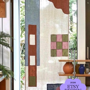 Könnte beinhalten: Ein rechteckiger Leinenvorhang mit cremefarbener Basis und verschiedenen geometrischen Stoffaufnähern in Blau, Rost, Olivgrün und Rosa. Das Design umfasst ein kariertes Quadrat und einen gewellten oberen Rand. Text: 2026 ETSY DESIGN AWARDS Finalist.