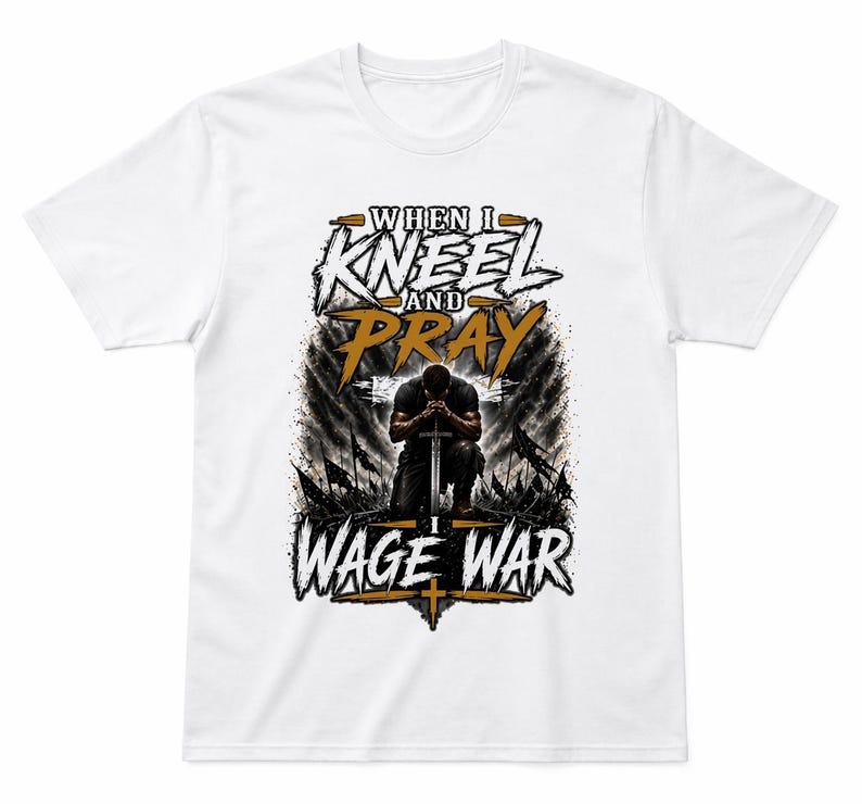 May include: White t-shirt featuring the text "WHEN I KNEEL AND PRAY I WAGE WAR" in a stylized design. The graphic includes a kneeling figure with a sword, set against a backdrop of flags and a cross.
