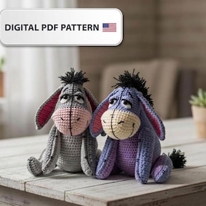 Peut inclure: Deux peluches d'ânes crochetées à la main, grises et violettes, avec des oreilles intérieures roses et des crinières noires, sont posées sur une surface en bois. Le texte "DIGITAL PDF PATTERN" est affiché au-dessus des jouets, avec une petite icône du drapeau américain.