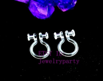 May include: Two clear, plastic clip-on earring converters. Each converter has a post and a curved, C-shaped loop. The text "ETSY ID: Jewelryparty" is visible. The background is black with a purple crystal.