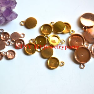 Peut inclure: Un assortiment de petits apprêts de bijoux ronds en métal, de tons dorés et cuivrés. Chaque apprêt est doté d'une petite boucle pour la fixation. Un cristal violet est visible en arrière-plan.