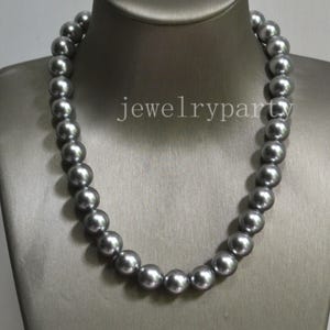 Puede incluir: Un collar de una sola hilera con perlas redondas y uniformes de color gris metálico con una superficie lisa y reflectante. Las perlas están ensartadas en una disposición circular continua. El texto "jewelryparty" es visible.