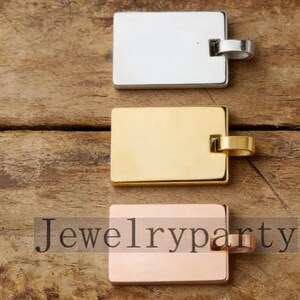 May include: Three rectangular metal pendants in silver, gold, and rose gold. Each pendant has a small loop attached to one end. The pendants are displayed on a wooden surface. The text "Jewelryparty" is visible.