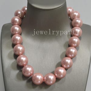 Könnte beinhalten: Eine einreihige Halskette mit großen, runden, glänzenden hellrosa Perlen mit glatter Oberfläche. Die Perlen sind einheitlich groß und kreisförmig aufgereiht. Der Text jewelryparty ist in der Mitte der Halskette zu sehen.