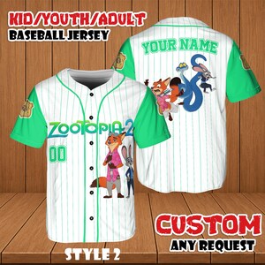 May include: White baseball jersey with green sleeves and trim, featuring the text "ZOOTOPIA 2" and the number "00". The jersey has cartoon characters on the front and back, with the text "YOUR NAME" on the back. The top reads "KID/YOUTH/ADULT BASEBALL JERSEY".