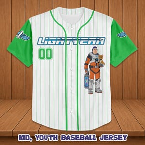 Puede incluir: Camiseta de b&eacute;isbol blanca con detalles verdes, con el texto azul "LIGHTYEAR" y el n&uacute;mero verde "00". La camiseta presenta un personaje de dibujos animados sosteniendo un gato. Las mangas son verdes con un logotipo blanco y azul.