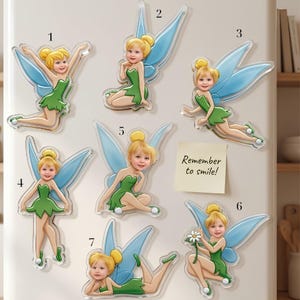 May include: Seven acrylic refrigerator magnets featuring a fairy character with blonde hair in a bun, a green dress, and blue wings. Each fairy has a different pose and a unique child's face. A square yellow note with the text Remember to smile is included.