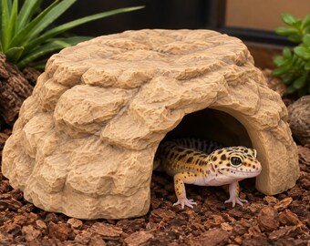 May include: A tan, textured reptile hide shaped like a rock formation with a hollow interior. A yellow and black spotted leopard gecko is positioned partially inside the opening of the structure, resting on a bed of dark brown wood chip substrate.