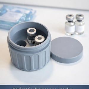 Puede incluir: Un contenedor gris para el almacenamiento y transporte de medicamentos con tapa, que contiene viales. El texto de la imagen dice "MEDICATION STORAGE & TRANSPORT CONTAINER".