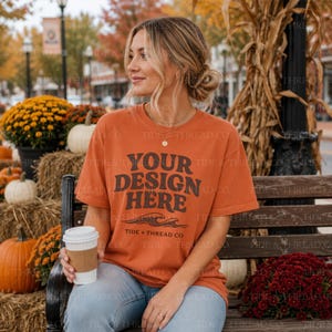 Op de afbeelding: Een roestoranje t-shirt met korte mouwen en de donkerbruine tekst "YOUR DESIGN HERE" in een vet, golvend lettertype, met een afbeelding van oceaangolven en de tekst "TIDE + THREAD CO" op de voorzijde van het kledingstuk.