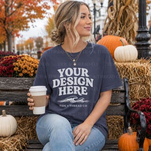 Op de afbeelding: Een donkerblauw T-shirt met korte mouwen en de witte tekst YOUR DESIGN HERE boven een afbeelding van twee oceaangolven en de tekst TIDE + THREAD CO. Het shirt wordt gedragen met een lichtblauwe spijkerbroek en een gouden ketting met hanger.