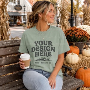 May include: A sage green short-sleeve t-shirt featuring dark gray text that reads YOUR DESIGN HERE with a graphic of ocean waves below the text and the brand name TIDE + THREAD CO printed in smaller letters underneath the wave illustration.
