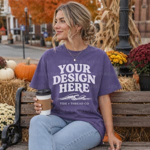 Op de afbeelding: Een paars t-shirt met korte mouwen en de witte tekst "YOUR DESIGN HERE" in een vet, golvend lettertype, geplaatst boven een afbeelding van oceaangolven en de tekst "TIDE + THREAD CO". Het t-shirt heeft een ronde hals en een relaxte pasvorm.