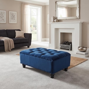 May include: A rectangular ottoman upholstered in deep blue velvet fabric featuring a tufted button design on the top surface. The piece is supported by four dark brown wooden feet with a rounded, turned shape, providing a stable base.