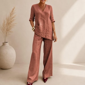 May include: A two-piece terracotta-colored linen outfit. The top has a V-neck and a single pocket. The wide-leg pants complete the ensemble. The outfit is suitable for casual or semi-formal occasions.
