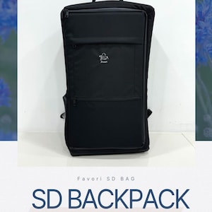 May include: Black SD backpack with multiple zippered compartments and a top handle. The backpack features the text "SD BACKPACK" and "BACKPACK FOR DOLL SIZE OVER 60cm". The backpack has a small logo on the front.