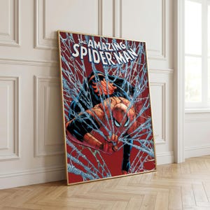 K&ouml;nnte beinhalten: Gerahmte Comic-Kunst mit Spider-Man in einer dynamischen Pose, umgeben von seinem Netz. Das Kunstwerk hat einen roten Hintergrund mit den Worten "The Amazing Spider-Man" oben. Der Rahmen ist goldfarben.
