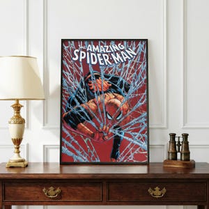 K&ouml;nnte beinhalten: Gerahmte Comic-Kunst mit Spider-Man, umgeben von seinem Netz. Der Titel "The Amazing Spider-Man" ist oben zu sehen. Das Kunstwerk hat einen roten Hintergrund und ist in einem schwarzen Rahmen.