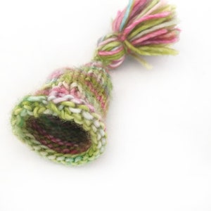 May include: A small, green, pink, and white knitted hat with a fluffy pom-pom.