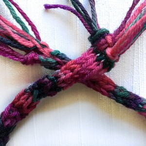 May include: A close-up of a multi-colored braided cord with pink, green, and purple yarn. The cord is tied in a knot.