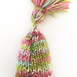 May include: A small, knitted hat with a green, pink, and white striped pattern. The hat has a matching tassel on top.