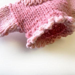 May include: A pink knitted sweater with a ruffled edge.