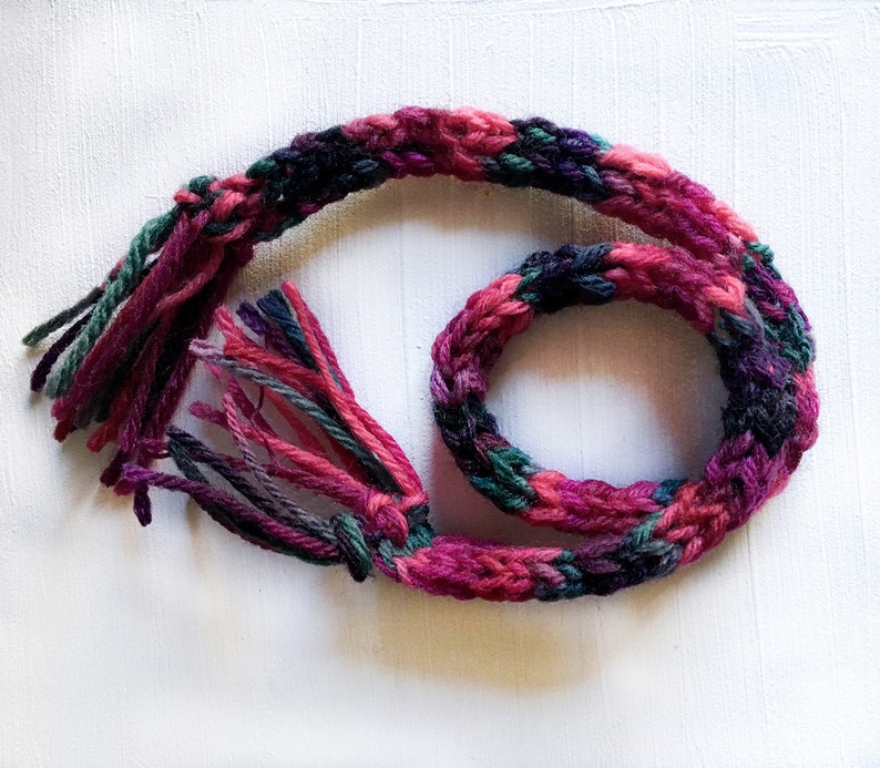 May include: A long, braided cord made of pink, green, and purple yarn with frayed ends.