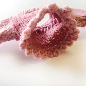 May include: A pink knitted sweater with a ruffled trim. The sweater is made of a soft, delicate yarn and has a loose, comfortable fit.