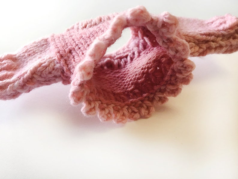 May include: A pink knitted sweater with a ruffled trim. The sweater is made of a soft, delicate yarn and has a loose, comfortable fit.