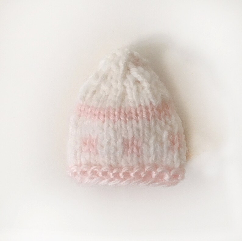 Puede incluir: Un gorro de beb&eacute; de punto blanco con rayas rosas y un borde rosa.