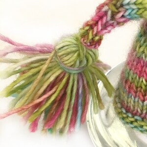 May include: A colorful knitted hat with a long tassel. The hat is made with a variety of shades of pink, green, and blue yarn.