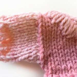 May include: Close-up of a pink knitted fabric with a textured pattern. The fabric is soft and fluffy, and the color is a light pink with a hint of white.