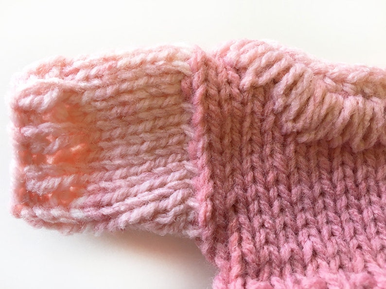 May include: Close-up of a pink knitted fabric with a textured pattern. The fabric is soft and fluffy, and the color is a light pink with a hint of white.