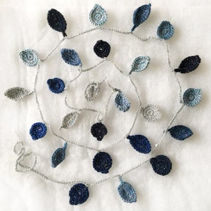 May include: A crocheted garland with blue and gray leaves. The garland is made of a silver thread and has a variety of different leaf shapes.