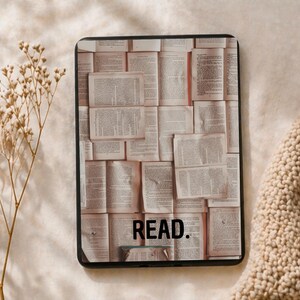 Könnte beinhalten: Eine schwarze rechteckige Hülle mit einer Collage aus offenen Buchseiten. Das Wort "READ." ist unten in Schwarz aufgedruckt. Die Hülle befindet sich vor einem neutralen, strukturierten Hintergrund mit einem Zweig getrockneter Blumen.
